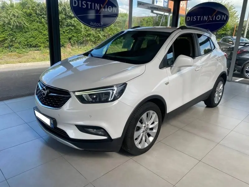 Opel Mokka blanc en 3/4 avant droit, avec jantes alliage et calandre noire brillante dans un showroom lumineux.