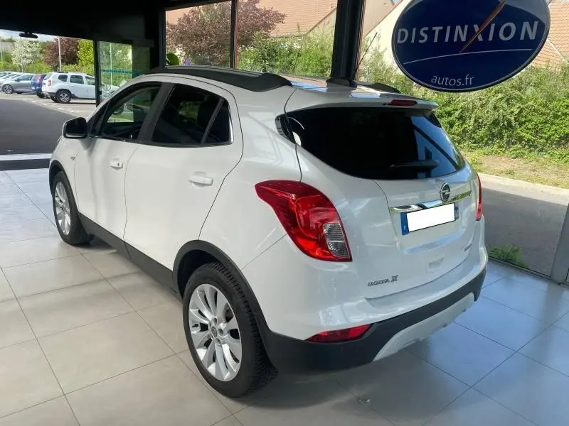 Vue 3/4 arrière droite d'un Opel Mokka blanc 2017 exposé en showroom avec vitres teintées et jantes alliage.