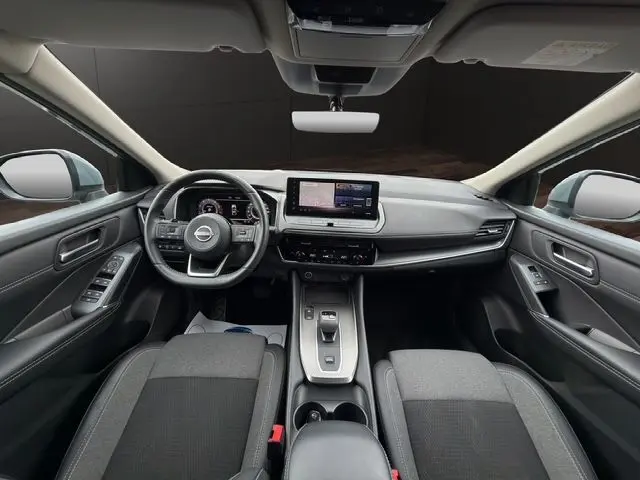 Vue intérieure avant du Nissan Qashqai 2025 en Ceramic Grey, tableau de bord moderne avec écran tactile central et volant multifonction.