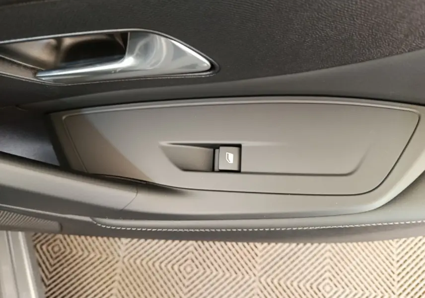 Détail de la commande de lève-vitre sur la porte intérieure côté conducteur d’une Peugeot 308 gris foncé 2026.