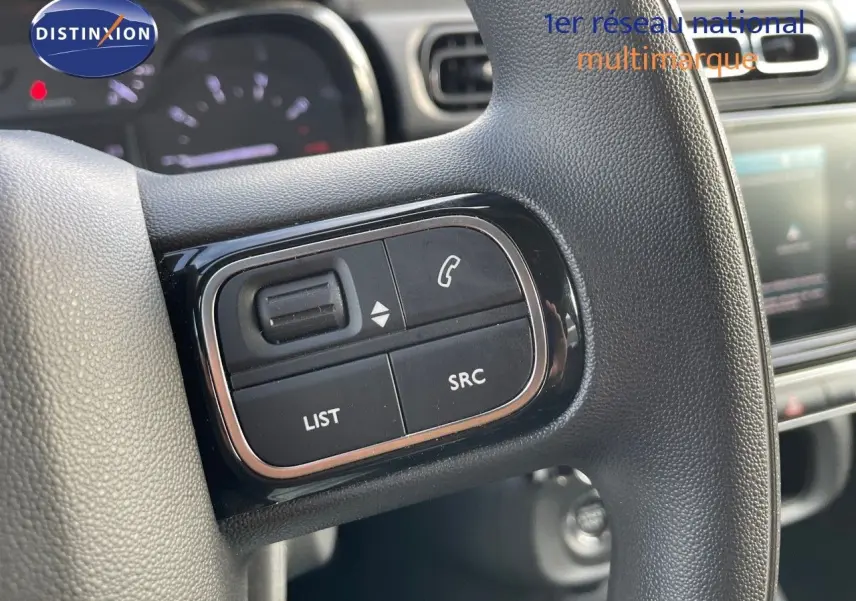 Gros plan sur les commandes multimédia noires à gauche du volant de la Citroën C3 gris platinium 2023.