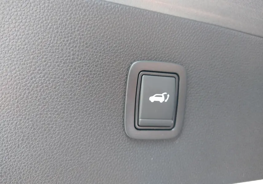 Bouton noir d'ouverture électrique du coffre sur panneau intérieur gris d'une Dacia Bigster 2025 gris schiste.