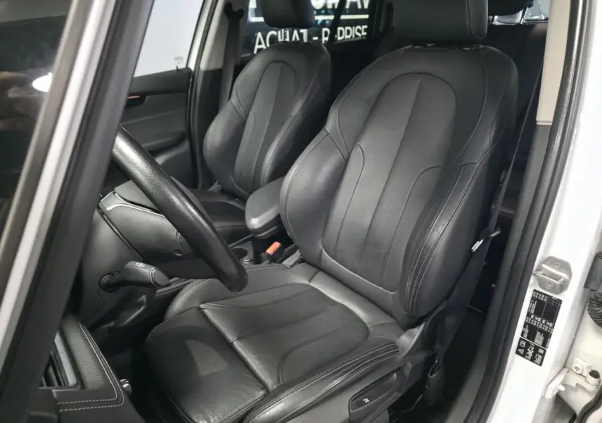 Vue intérieure côté conducteur de la BMW Série 2 Gran Tourer 218d xDrive blanche avec sièges cuir noirs et volant sport.