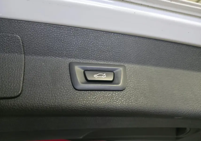 Bouton d'ouverture électrique du hayon sur le bord intérieur du coffre d'une BMW Série 2 blanc.