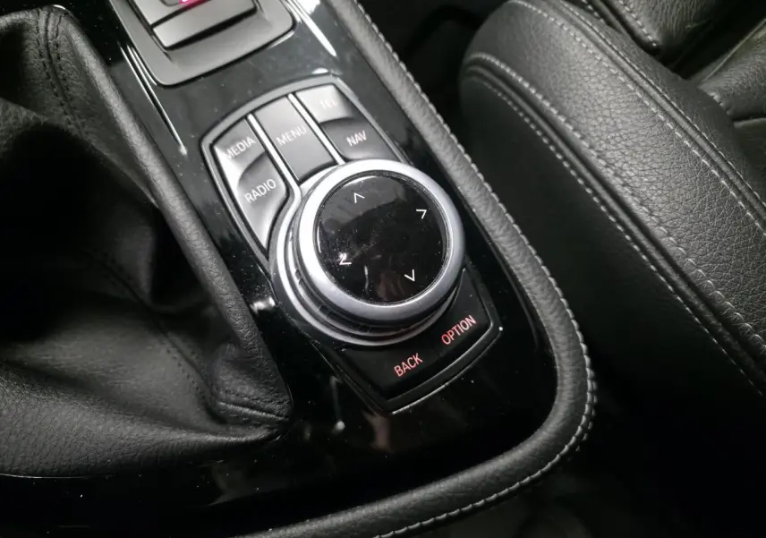 Gros plan sur la molette de commande iDrive noire et argentée, entourée de cuir noir sur la console centrale d'une BMW Série 2 Gran Tourer.