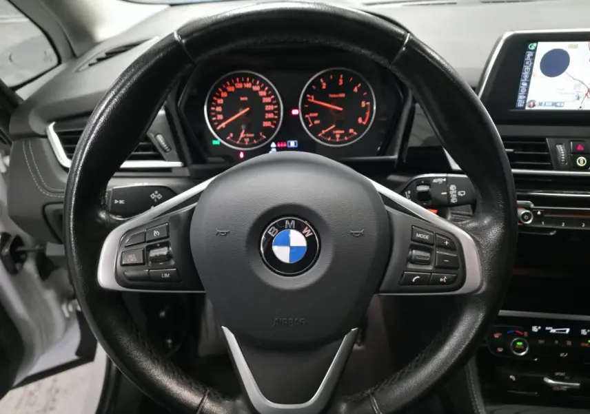 Vue rapprochée du volant cuir noir et du tableau de bord éclairé d'une BMW Série 2 Gran Tourer blanche de 2016.