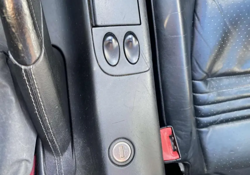 Gros plan sur la console centrale noire et le siège en cuir perforé côté conducteur d'une Porsche 911 Targa gris foncé 2004.