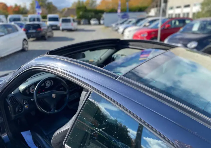 Vue 3/4 côté gauche d'une Porsche 911 Targa 3.6i gris foncé 2004 avec toit ouvert et intérieur visible.