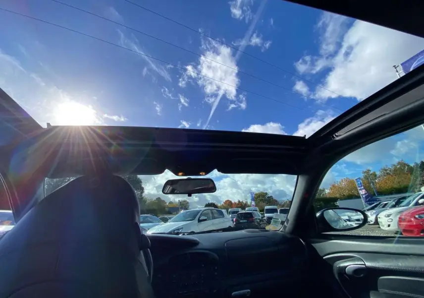 Vue intérieure avant d'une Porsche 911 Targa gris foncé de 2004, avec toit ouvert sous un ciel bleu lumineux.