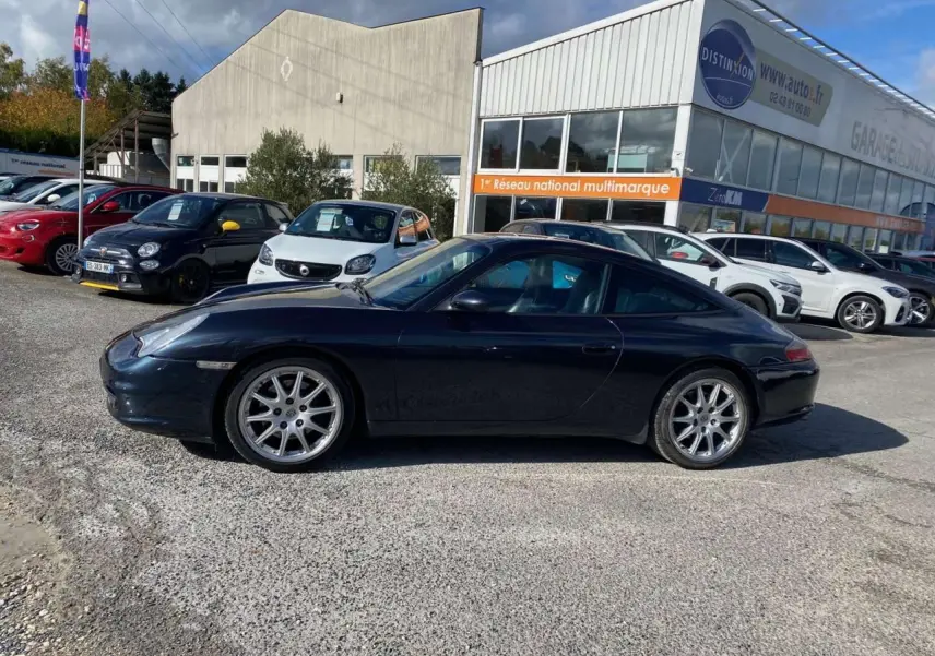 Profil côté gauche d'une Porsche 911 Targa 3.6i gris foncé de 2004 garée en extérieur sur un parking.