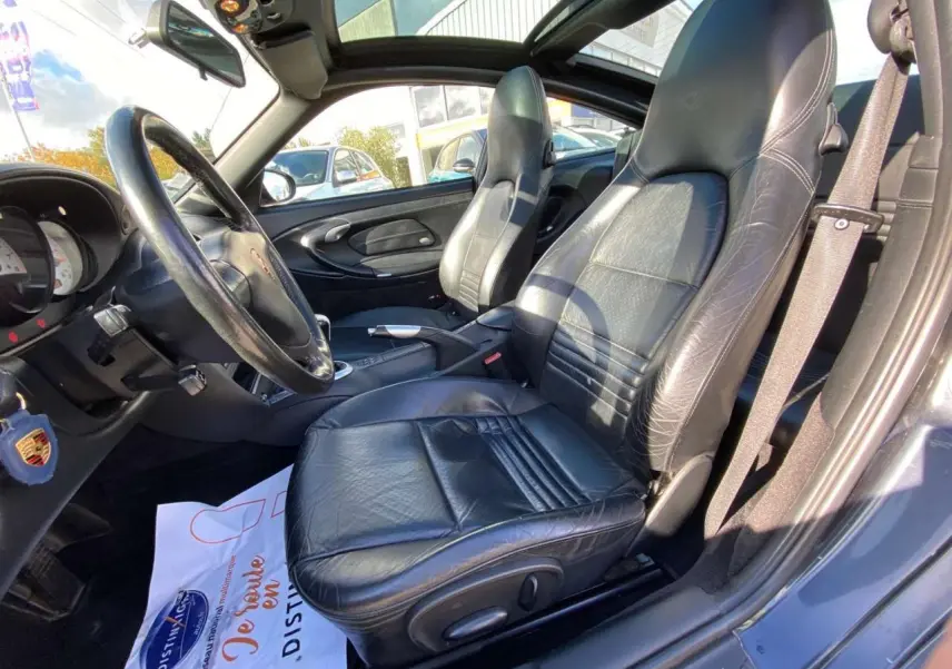 Intérieur côté conducteur d'une Porsche 911 Targa 2004 gris foncé, sièges cuir noir et volant sport visible.