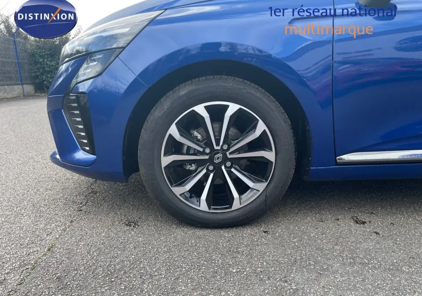 Gros plan sur la roue avant gauche et l'aile d'une Renault Clio TCE 90CH TECHNO bleu iron metal, avec jante alliage bicolore.