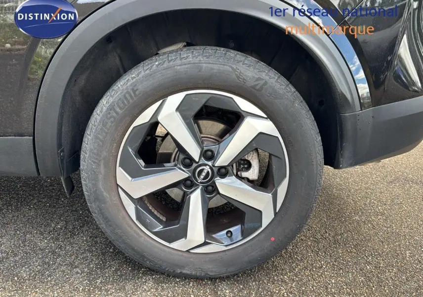 Gros plan sur la roue avant gauche du Nissan Qashqai noir 2024, mettant en valeur la jante alliage bicolore au design moderne.