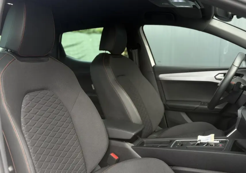 Vue intérieure côté droit du SEAT LEON 2024 avec sièges tissu noir à surpiqûres orange et console centrale moderne.