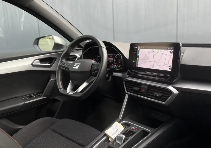 Intérieur côté conducteur du SEAT Leon blanc 2024, volant cuir multifonction et écran tactile de navigation visible