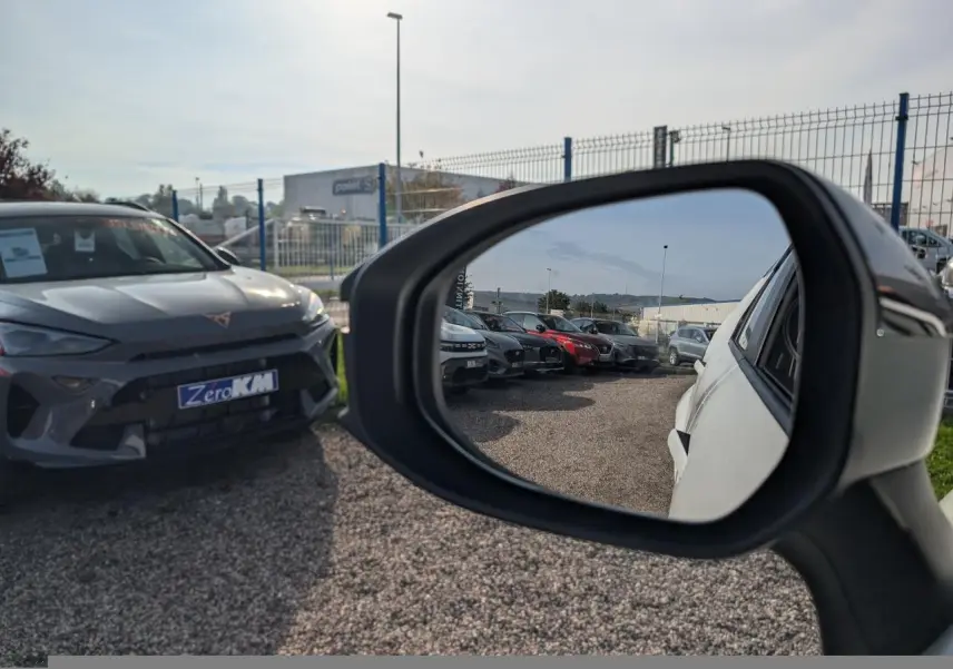Rétroviseur droit montrant la carrosserie blanche du Toyota C-HR 2024 en partie, avec vue sur un parking de voitures.