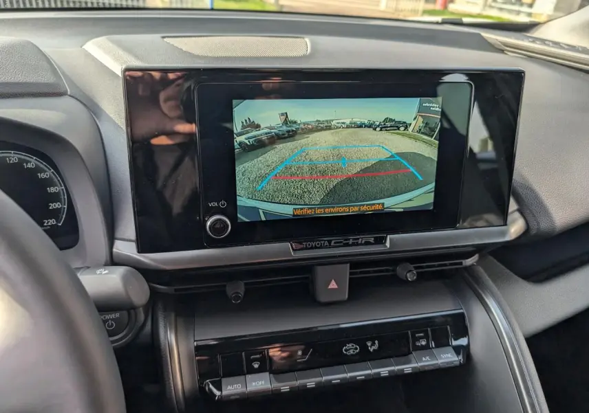Vue intérieure centrée sur l'écran tactile affichant la caméra de recul du Toyota C-HR blanc, tableau de bord visible.