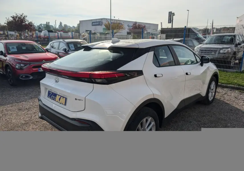Toyota C-HR blanc vu en 3/4 arrière droit, avec feux arrière full LED et poignées affleurantes noires.