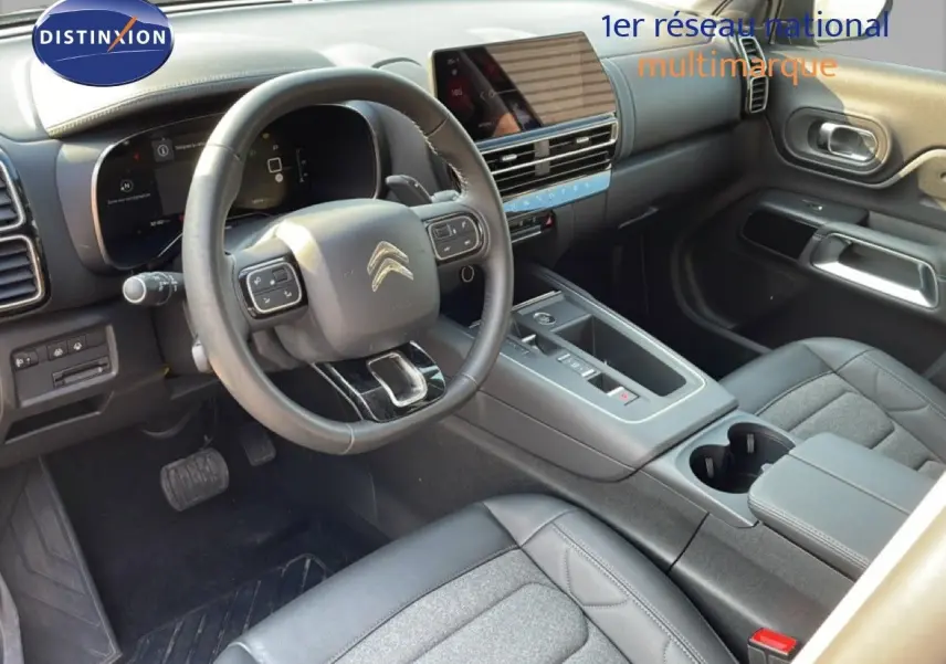 Vue intérieure du poste de conduite du Citroën C5 Aircross 2025, avec volant multifonction et sellerie tissu cuir gris-noir.