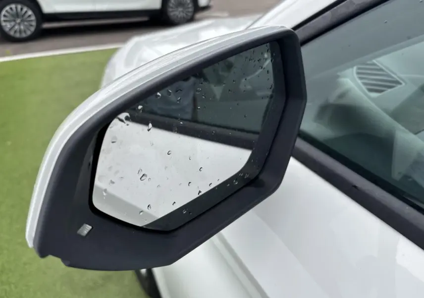 Rétroviseur côté gauche blanc de la SEAT LEON IV 1.5 TSI 130CH STYLE PACK 2024 avec gouttes de pluie visibles.