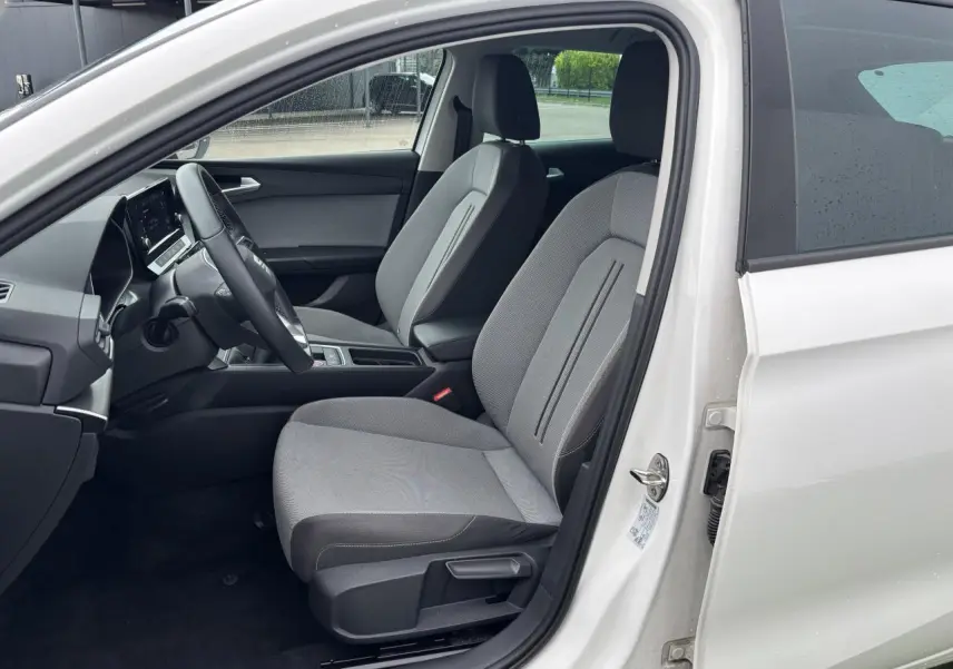 Intérieur côté conducteur d'une SEAT LEON blanche 2024, montrant les sièges gris et le volant multifonction cuir.