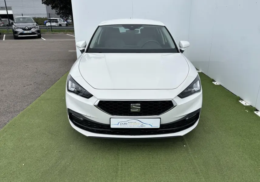 Vue frontale d'une SEAT Leon IV blanche avec calandre noire hexagonale et projecteurs Full LED, stationnée sur sol vert.
