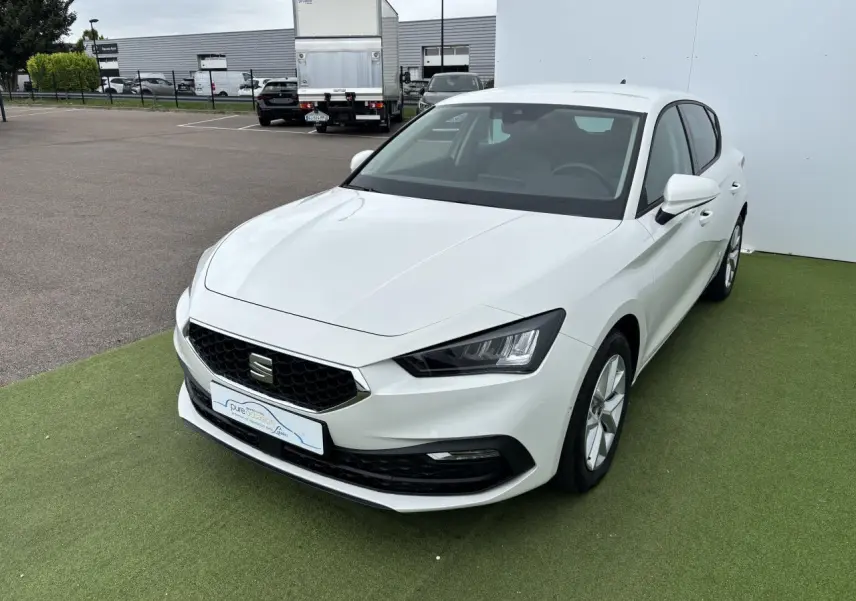 SEAT Leon IV blanche vue en 3/4 avant droit, avec calandre noire et jantes alliage 16 pouces sur fond vert.