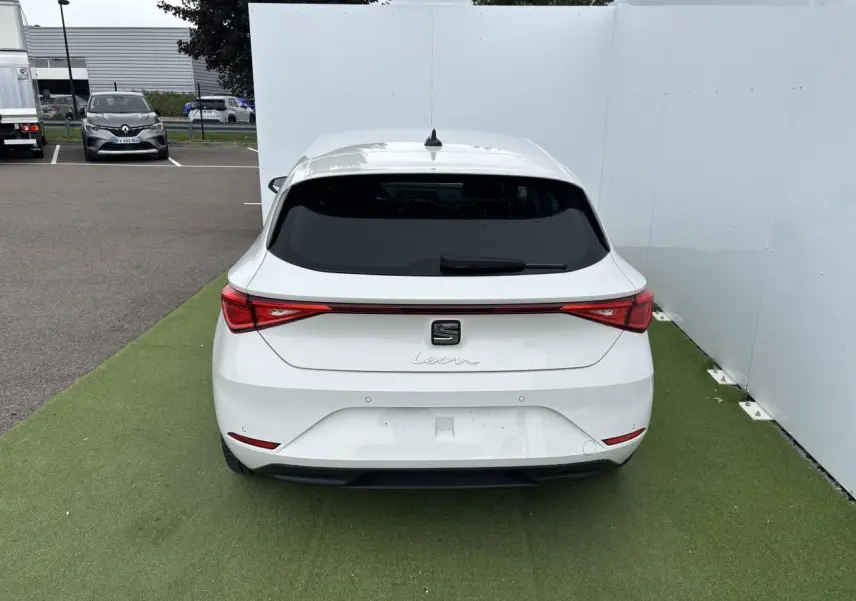 Vue arrière d'une SEAT Leon blanche 2024 garée sur sol vert avec feux arrière LED et lunette arrière teintée.
