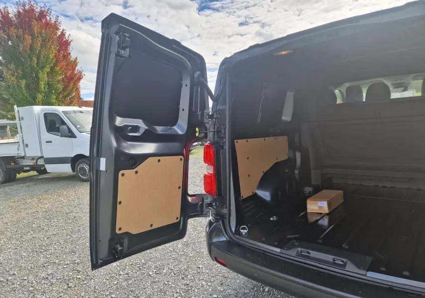 Vue arrière du Citroën Jumpy XL gris titane avec portes ouvertes montrant l'espace de chargement vide et un carton posé à l'intérieur.