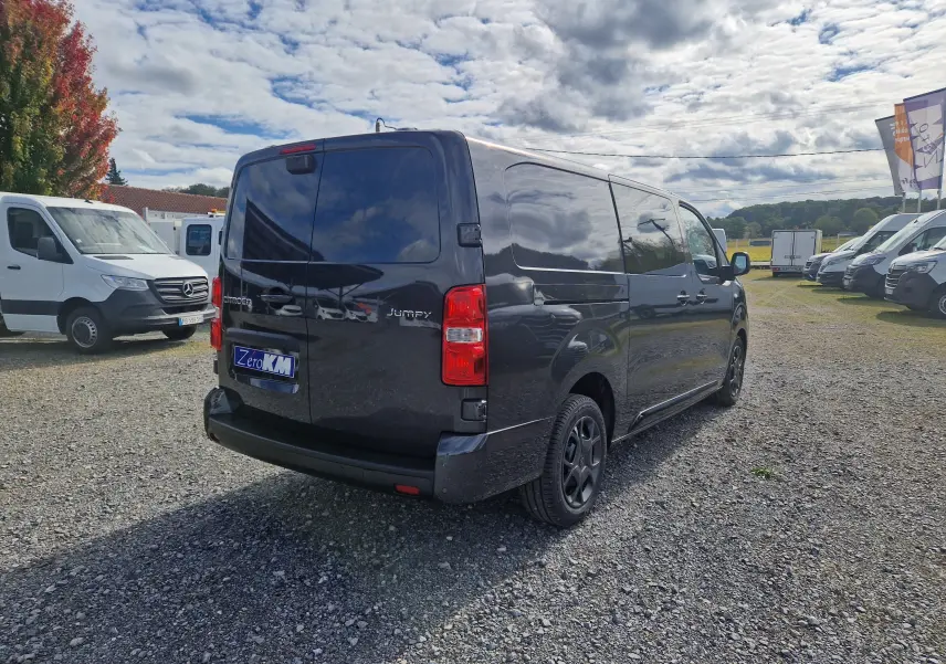 Vue 3/4 arrière droite d'un Citroën Jumpy cabine approfondie gris titane avec jantes tôles 17 pouces sur parking extérieur.
