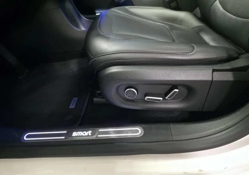 Gros plan sur le siège conducteur noir cuir et le seuil de porte blanc éclairé du logo Smart d'une Smart #1 électrique 2024.