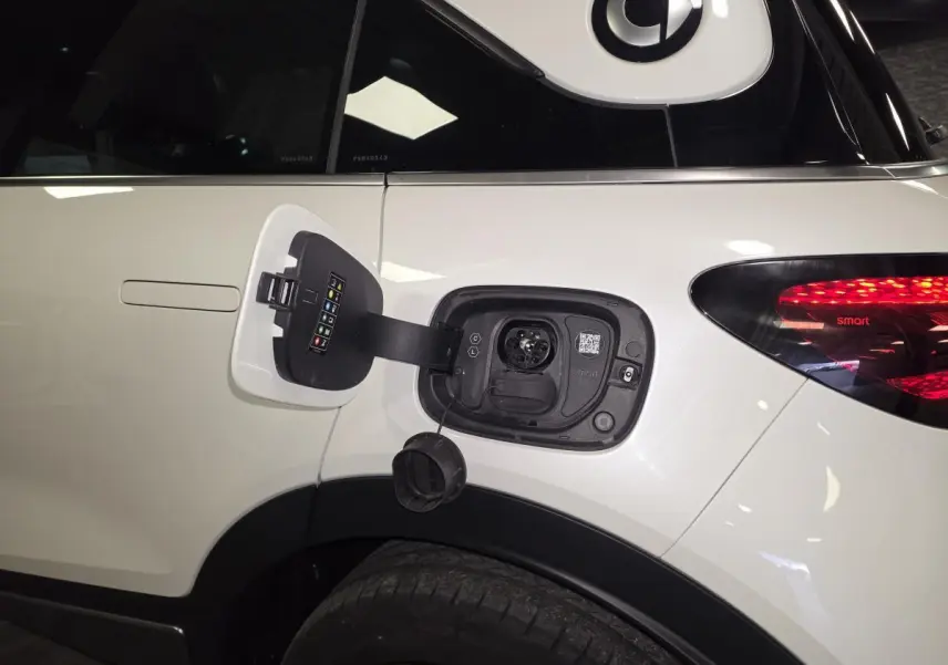 Prise de recharge électrique ouverte sur le côté gauche arrière d'une Smart #1 blanche avec feu arrière allumé.