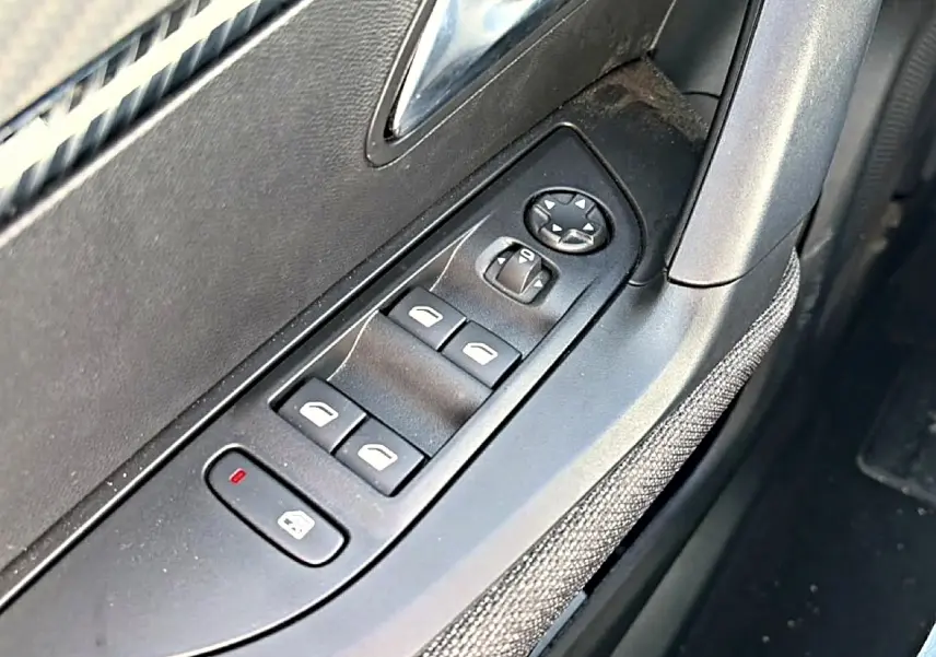 Gros plan sur la commande des vitres électriques côté gauche d'une Peugeot 2008 gris, avec tissu Renzo visible sur la portière.