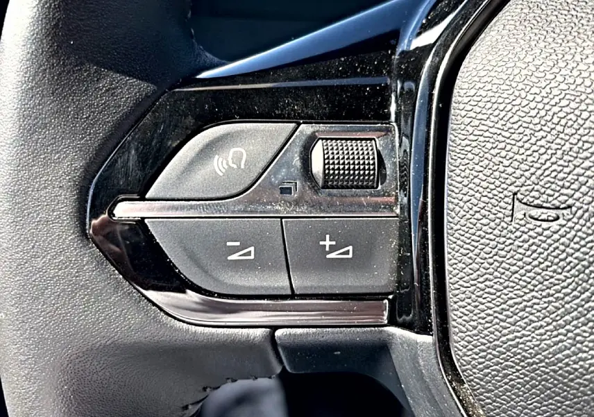 Gros plan sur les commandes de volume et appel vocal sur le volant noir du Peugeot 2008 gris 2025.
