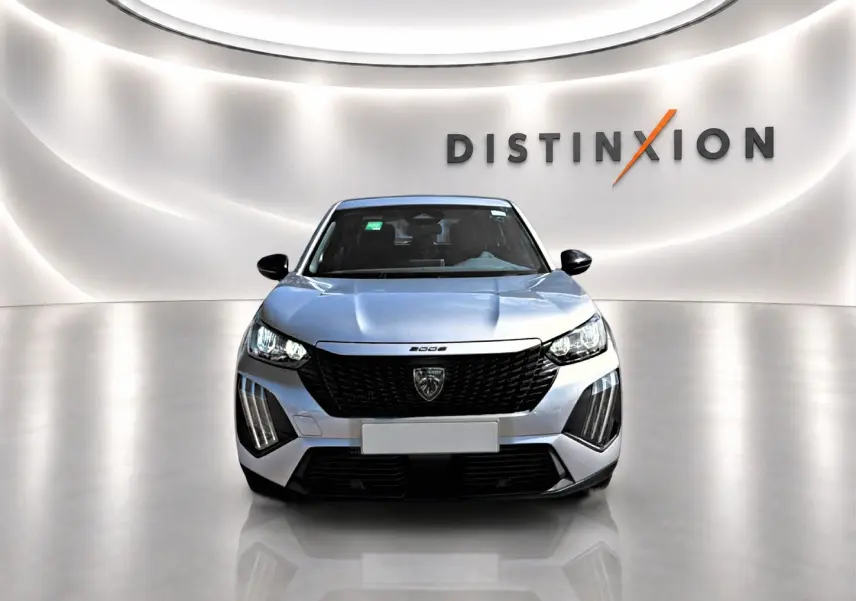 Vue frontale d'un Peugeot 2008 gris 2025 avec calandre noire et phares LED, dans un showroom lumineux.