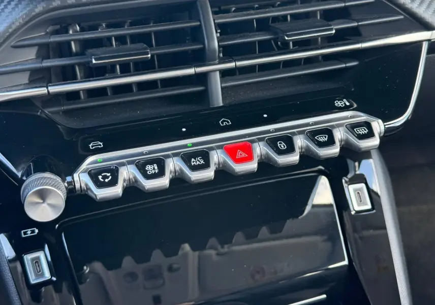 Vue rapprochée de la console centrale noire brillante de la Peugeot 208 1.2 100ch Allure avec boutons argentés et rouge d’alerte.