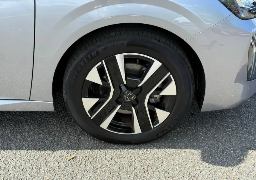 Gros plan sur la roue avant droite d'une Peugeot 208 2025 gris Artense avec jante alu bicolore moderne.