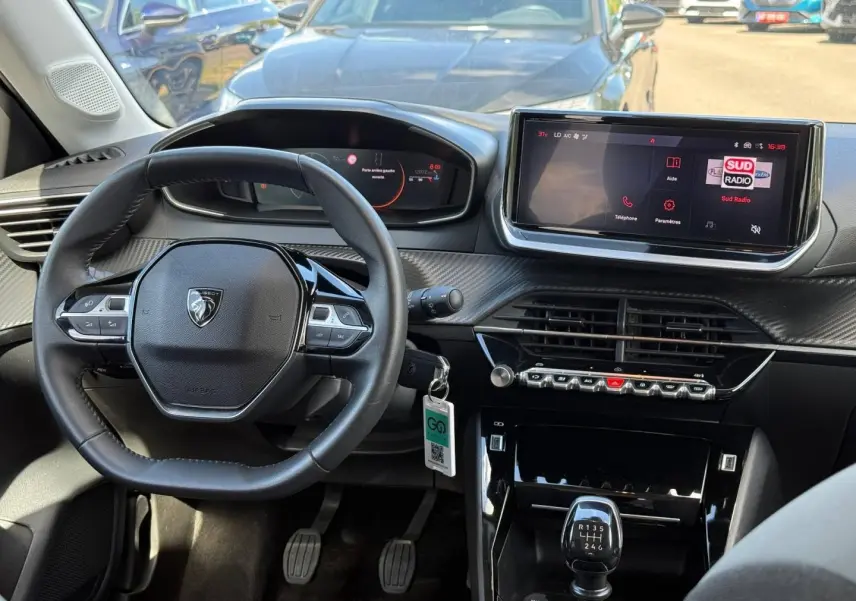 Vue intérieure avant centrée sur le volant compact et l'écran tactile du tableau de bord d'une Peugeot 208 gris Artense.