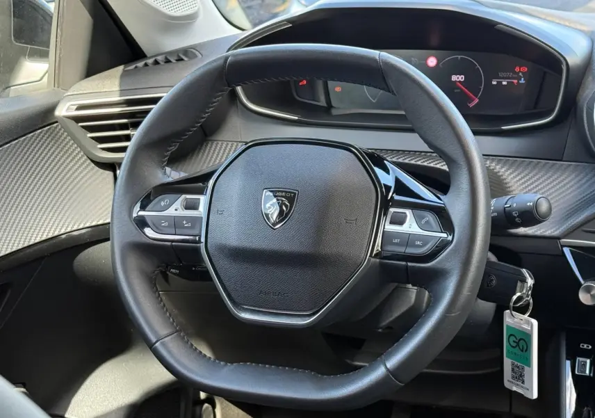 Vue rapprochée du volant noir du Peugeot 208 2025 avec tableau de bord numérique et commandes intégrées.