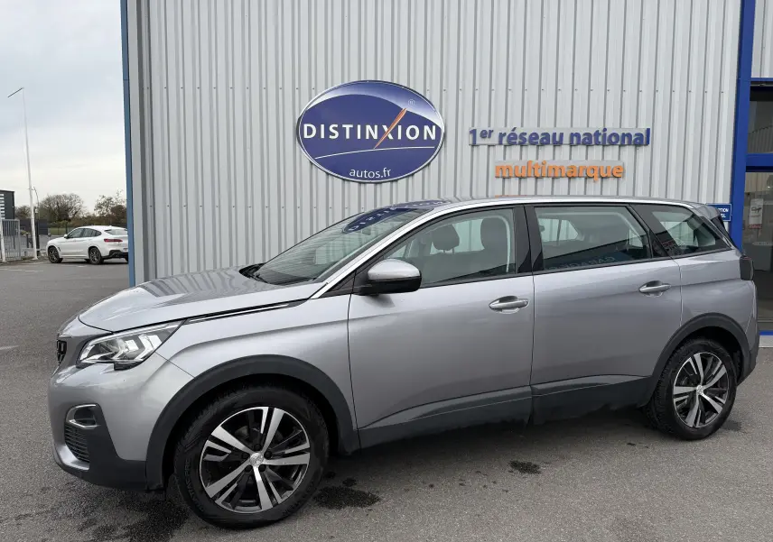 Peugeot 5008 gris Artense vue de profil côté gauche, stationnée devant un bâtiment avec enseigne Distinxion.