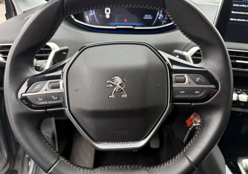 Vue rapprochée du volant cuir noir du Peugeot 5008 2020, avec commandes intégrées et logo lion central argenté.