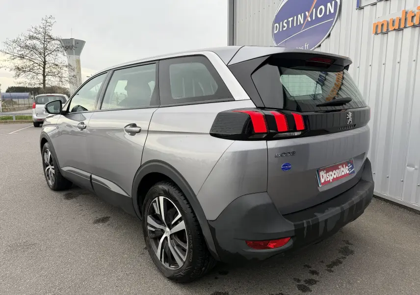 Vue 3/4 arrière droite d'un Peugeot 5008 gris Artense avec feux arrière à griffes rouges et jantes alliage.