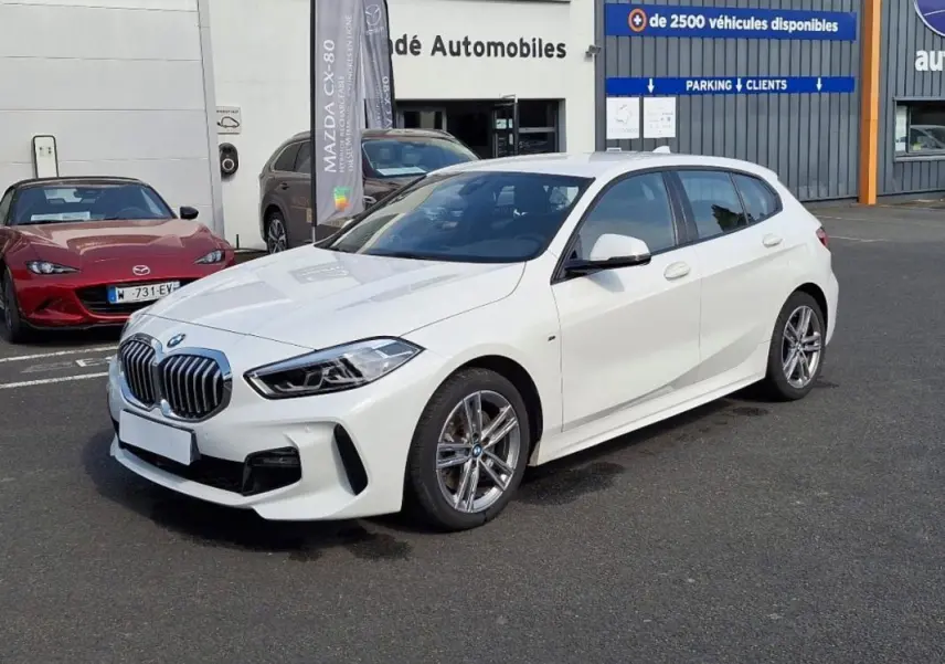 BMW Série 1 120i M Sport blanc vue 3/4 avant droit, avec jantes aluminium et calandre imposante.