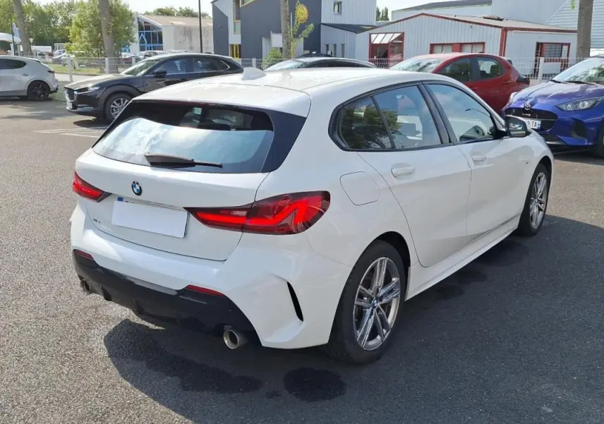 BMW Série 1 blanche vue en 3/4 arrière droit, avec jantes aluminium et feux arrière LED distinctifs.