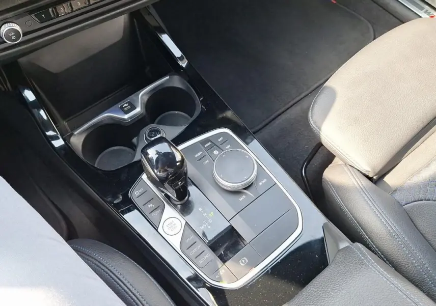 Gros plan sur la console centrale noire brillante de la BMW Série 1 120i M Sport avec levier de vitesse automatique et accoudoir cuir beige.
