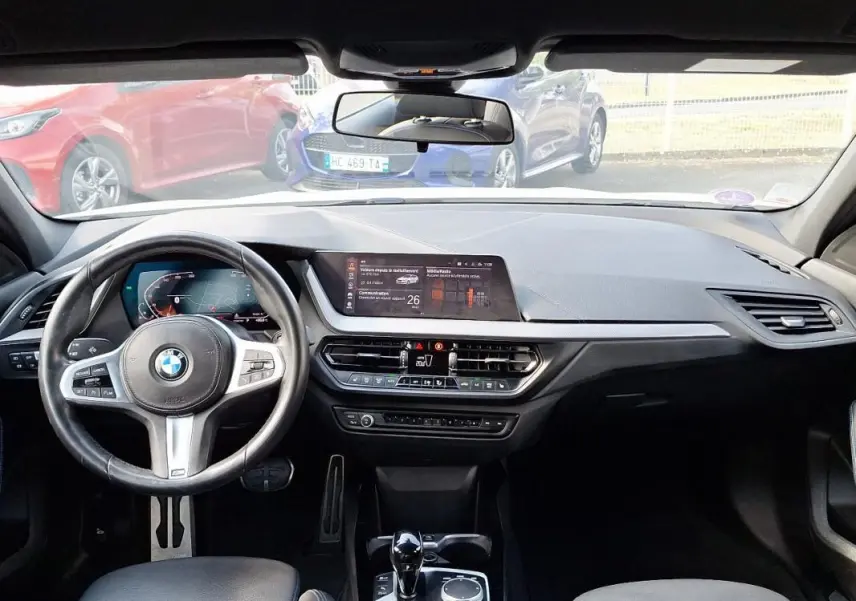 Vue intérieure de la BMW Série 1 120i M Sport 2021, tableau de bord et volant cuir multifonctions noirs.
