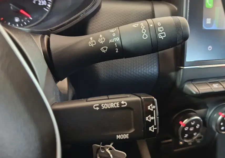 Gros plan sur les commandes au volant de la Renault Clio gris clair 2023, avec levier d'essuie-glace et multimédia.