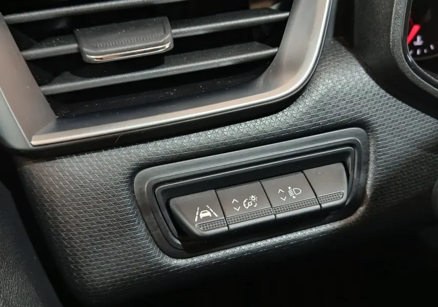 Gros plan sur les commandes d'assistance à la conduite et réglage des phares dans l'habitacle noir de la Renault Clio gris clair.