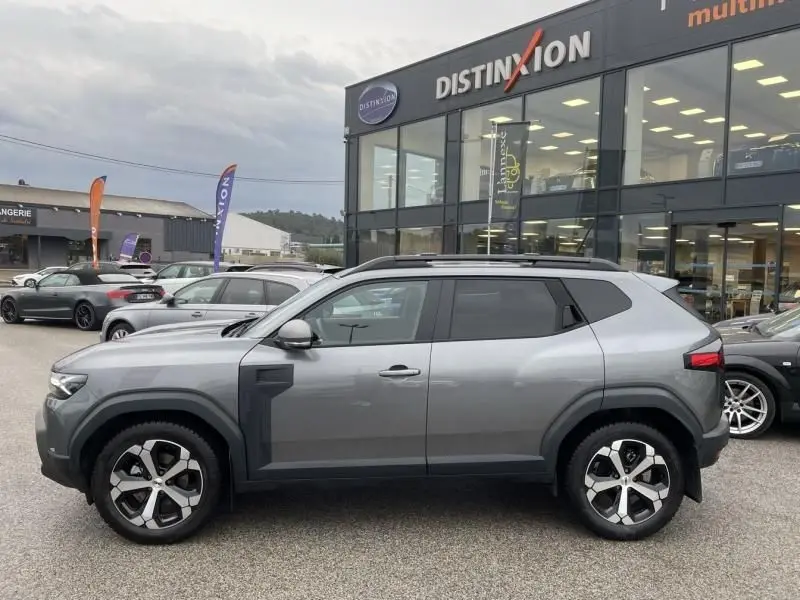 Vue de profil côté gauche du Dacia Duster 1.6 Hybrid gris schiste 2025 avec jantes distinctives et toit noir.