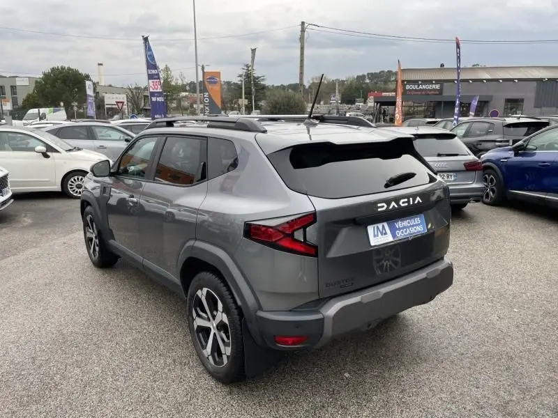 Vue 3/4 arrière droite d'un Dacia Duster 1.6 Hybrid gris schiste avec jantes alliage et toit noir, stationné en extérieur.